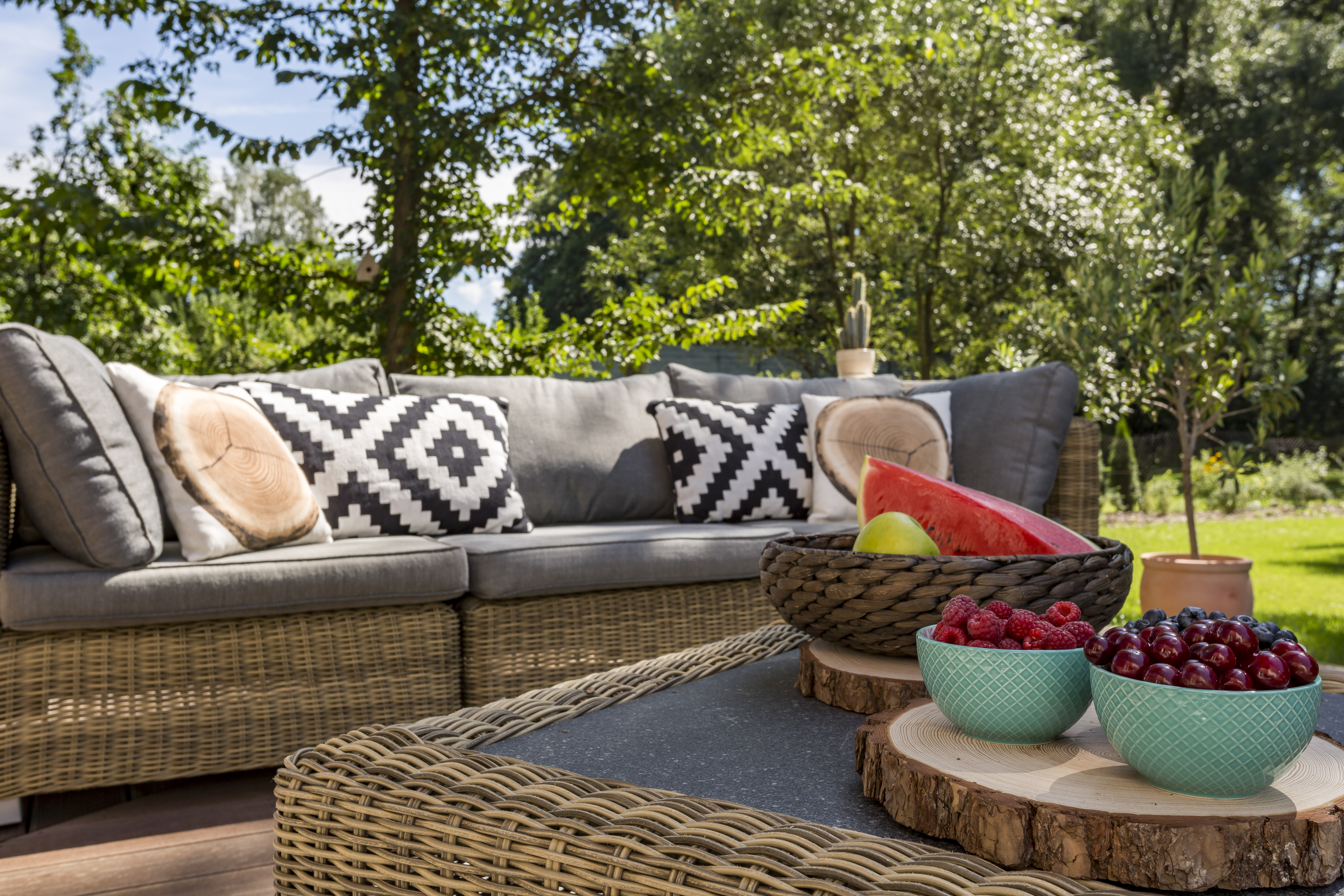 Image of an outdoor rattan sofa and coffee table, trees in the background